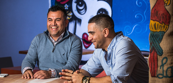 Juan Carrillo and Jason Méndez sitting at a table, smiling
