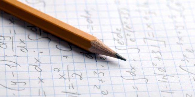 Close-up of a sharpened pencil with math equations on graph paper in the background