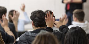 Back of several heads in a classroom, with some hands raised