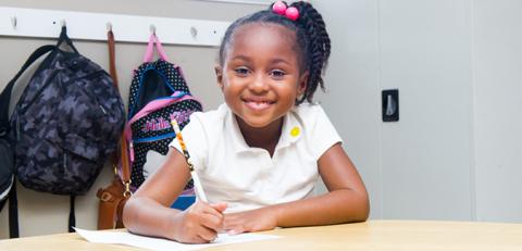 Young girl smiling while writing with a pencil